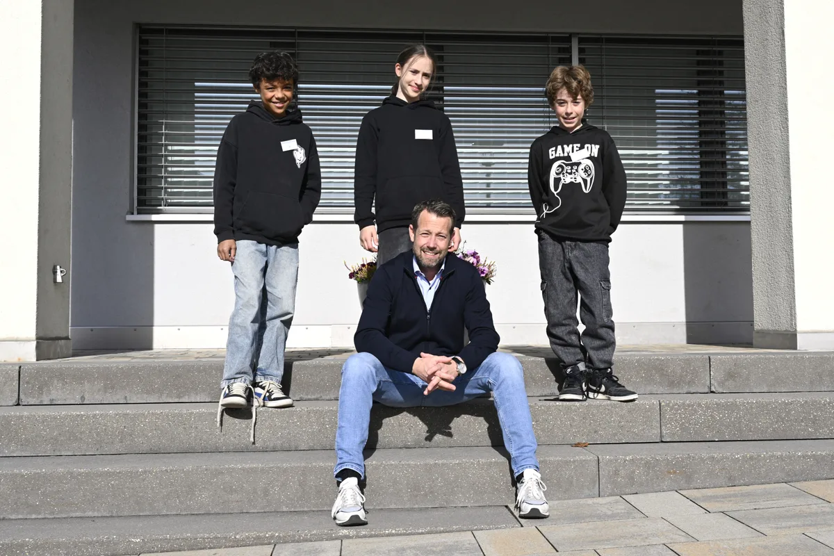 Drei Jugendliche stehen hinter einem Mann, der wiederum auf diener Treppe sitzt.